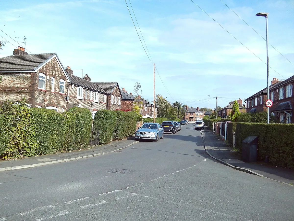 Red-brick terraced and semi-detached houses behind hedges on Heathwood Road in Burnage