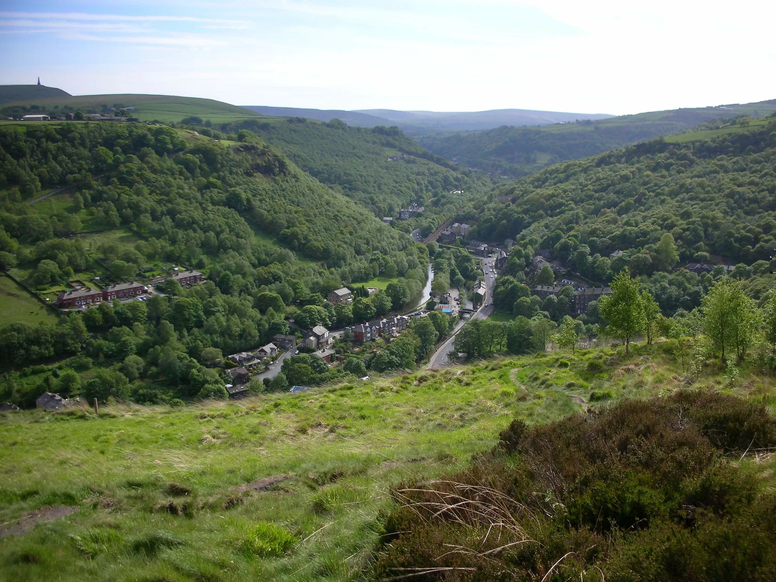 The wooded Calder Valley below Heptonstall, with stone houses along the valley floor and Stoodley Pike on the skyline